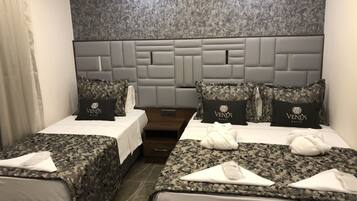 Habitación de hotel con dos camas, cada una con cubrecama y almohadas a cuadros de camuflaje. El cabecero presenta un diseño moderno con acabado gris texturizado.
