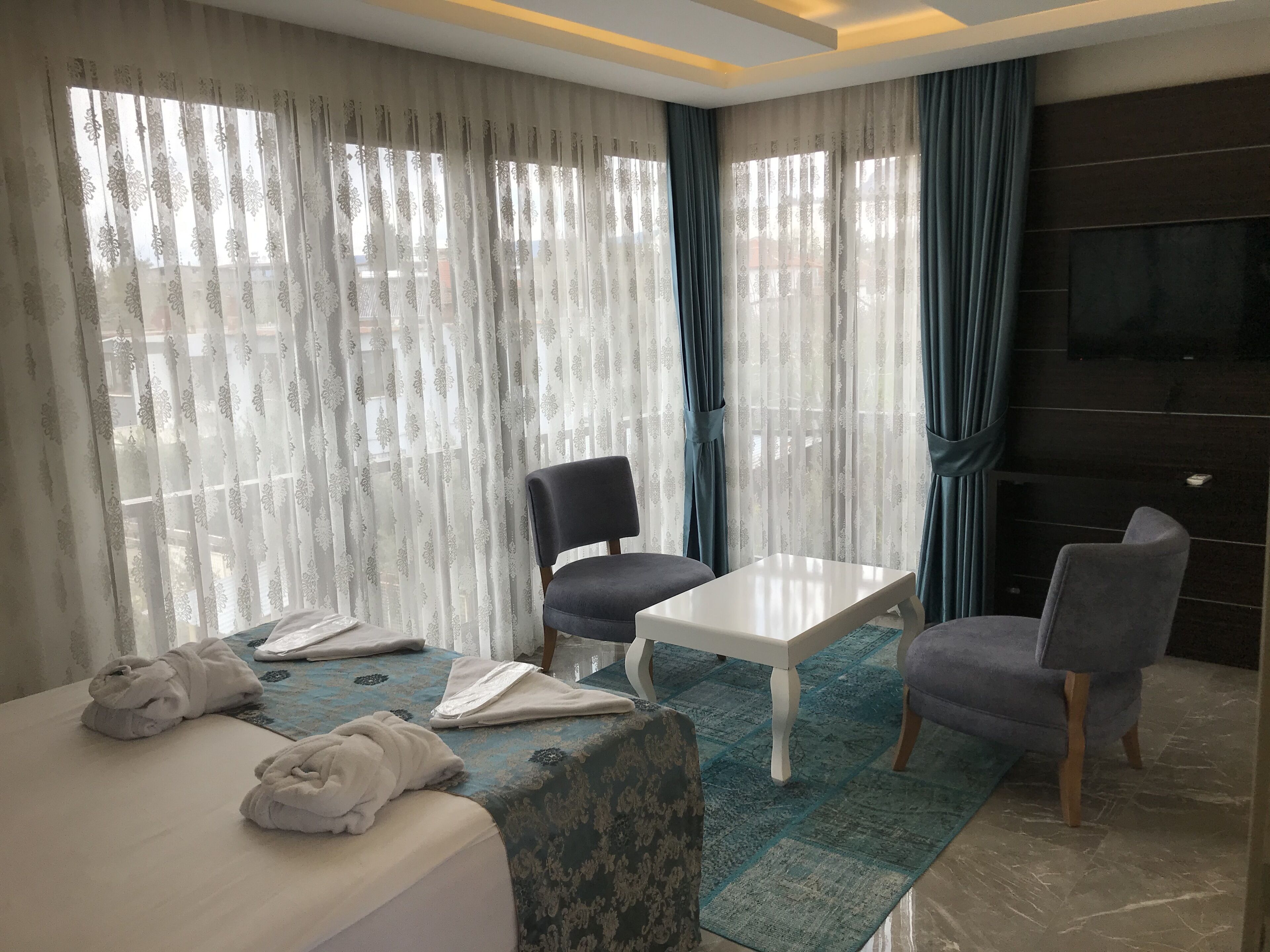 A hotel room with a bed, two chairs, a small table, and a TV on the wall.