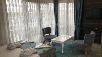 A hotel room with a bed, two chairs, a small table, and a TV on the wall.