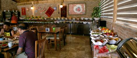 Un comedor con mesas y sillas de madera, un bufé con diferentes opciones de comida y una pared de ladrillo con detalles decorativos.