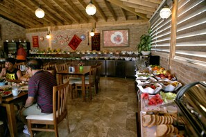 A dining area with wooden tables and chairs, a buffet with various food items, and a brick wall with decorative elements. - Venus Hotel (Denizli)