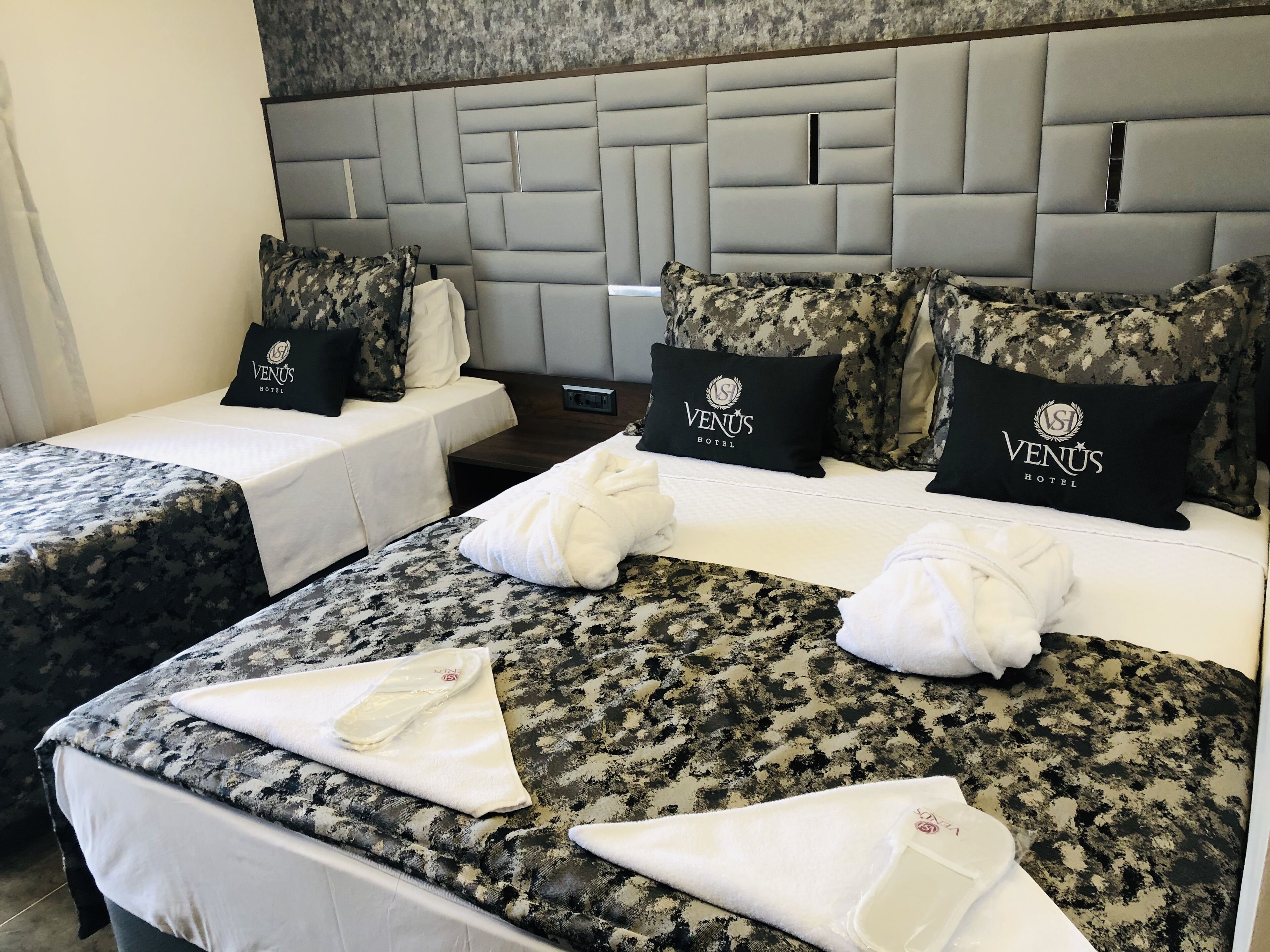 Une chambre d’hôtel avec deux lits, chacun agrémenté d’une couvre-lit à motifs et de coussins assortis. La chambre est dotée d’une tête de lit moderne et d’une petite table de chevet avec une lampe.