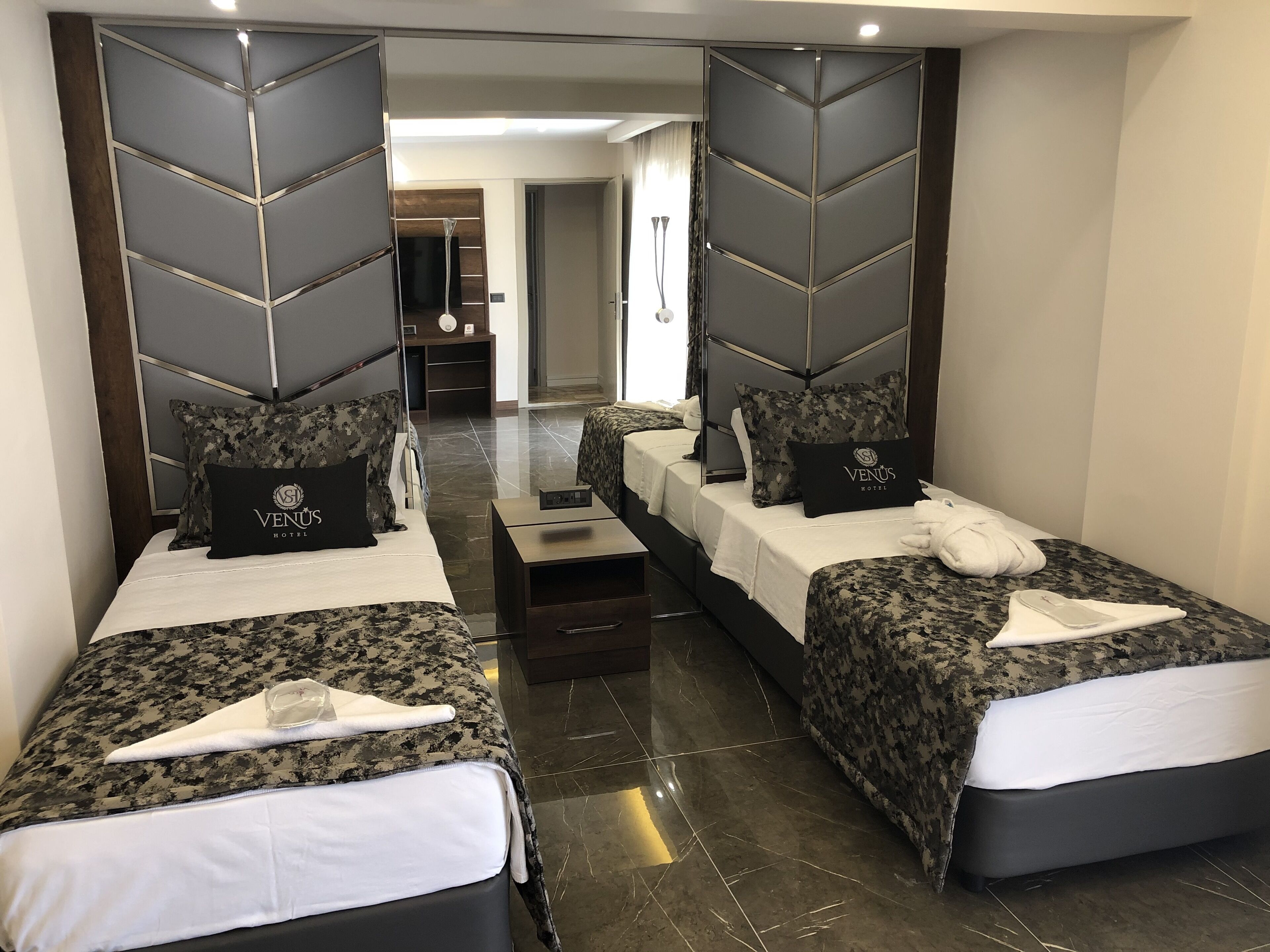 Una habitación de hotel con dos camas, cada una con un almohadón y una manta. Hay una pequeña mesa entre las camas.