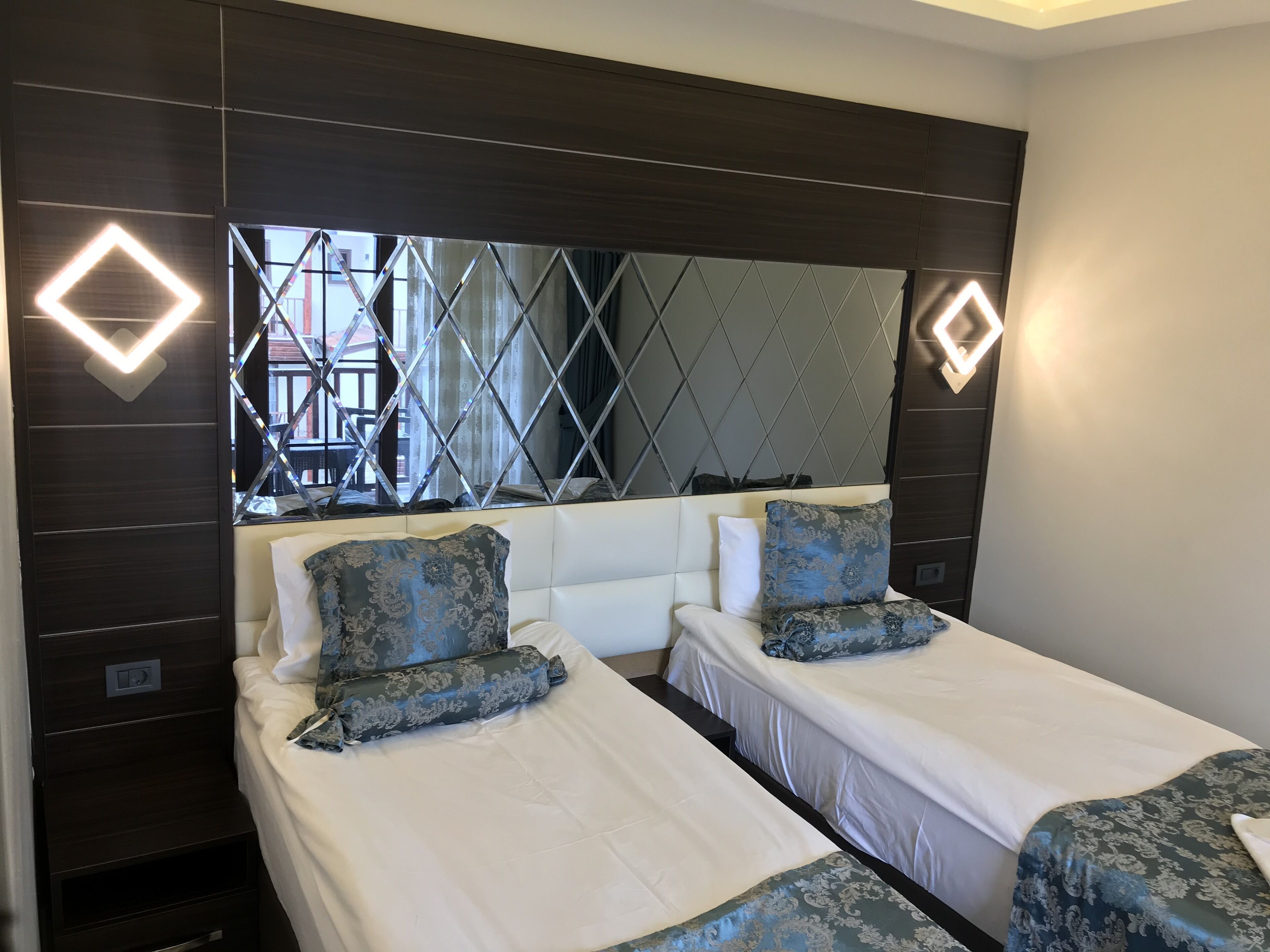A hotel room with two beds, dark wooden headboard, and a large mirror.