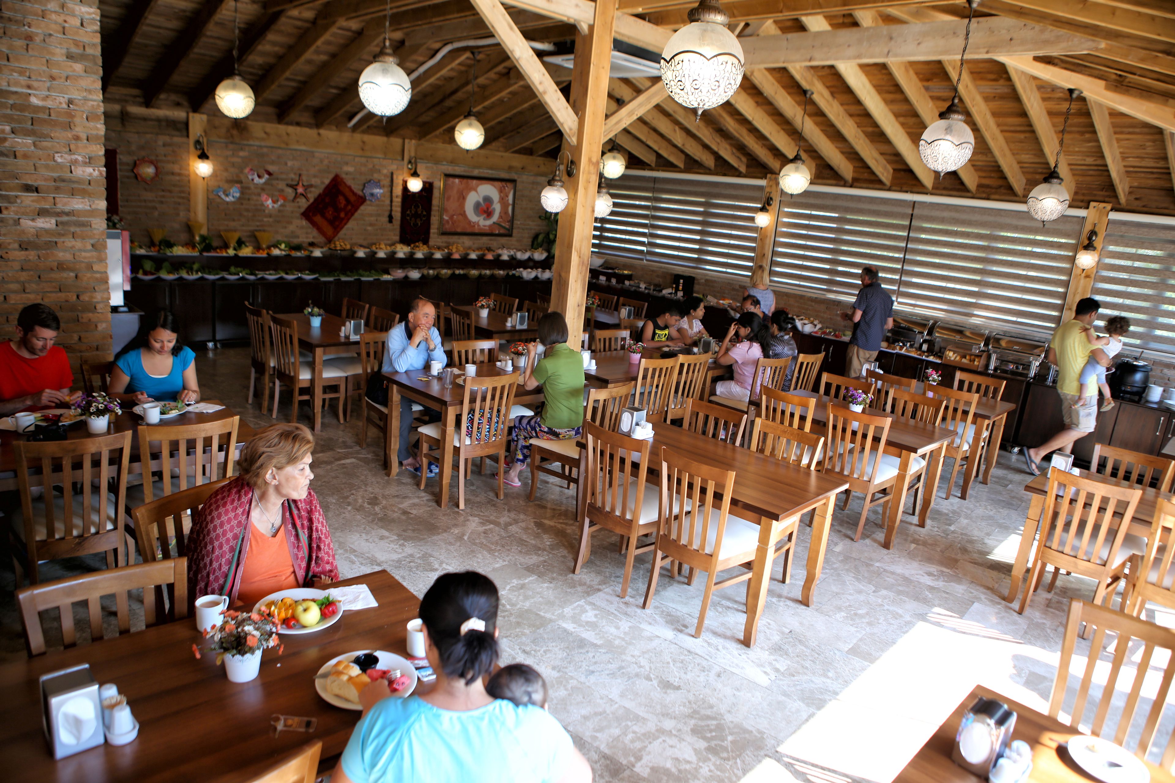 A restaurant with wooden tables and chairs, a brick wall, and hanging light fixtures.