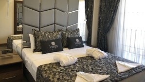 A hotel room with a modern design, featuring a large bed with a patterned bedspread, two pillows with the hotel logo, a headboard with geometric patterns, and a large mirror. - Venus Hotel (Denizli)
