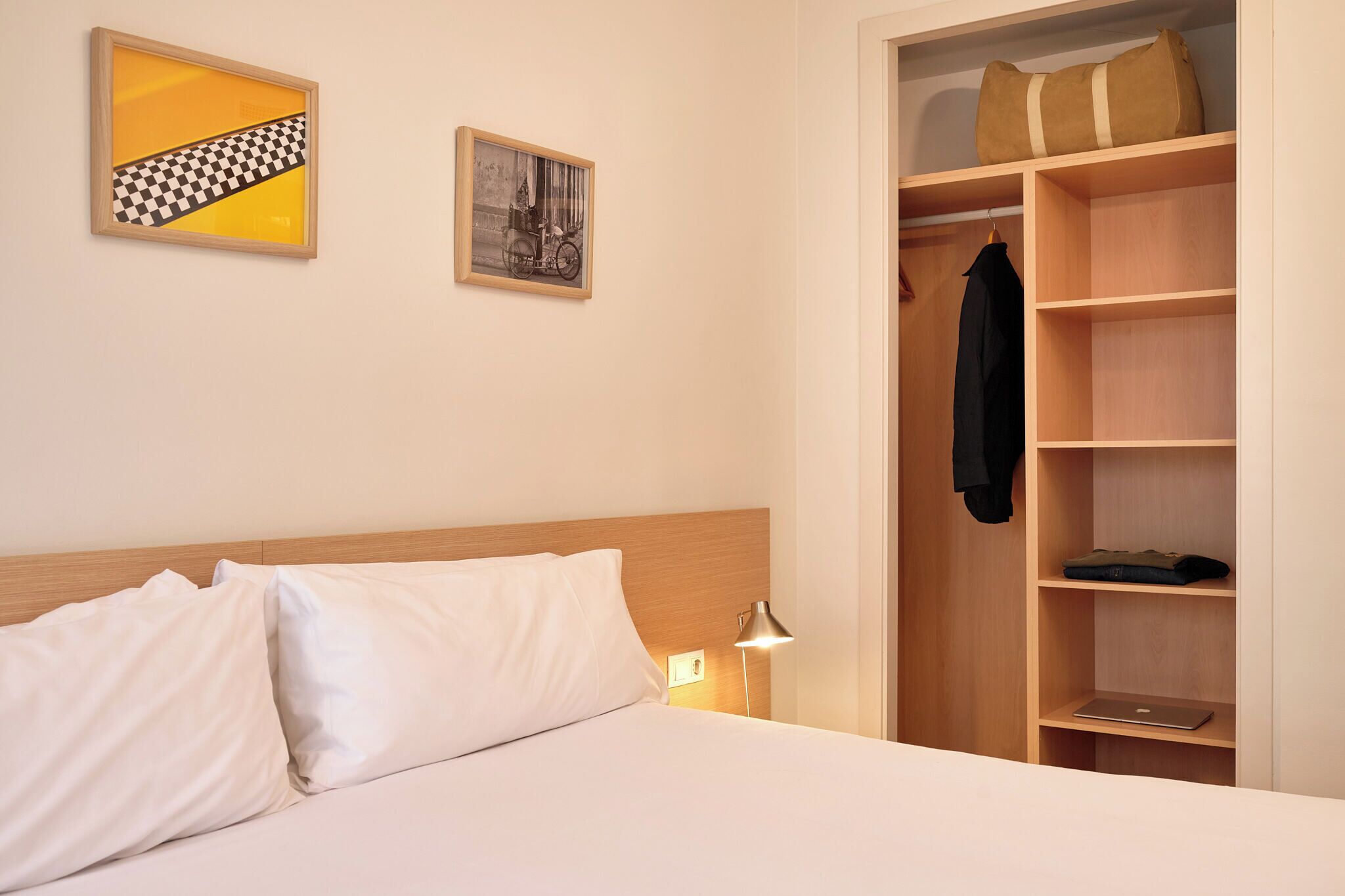 A hotel room with a bed, a wardrobe, and two framed pictures on the wall.