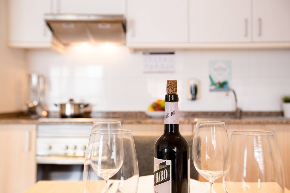 Una botella de vino y cuatro copas de vino vacías sobre una mesa en una cocina.