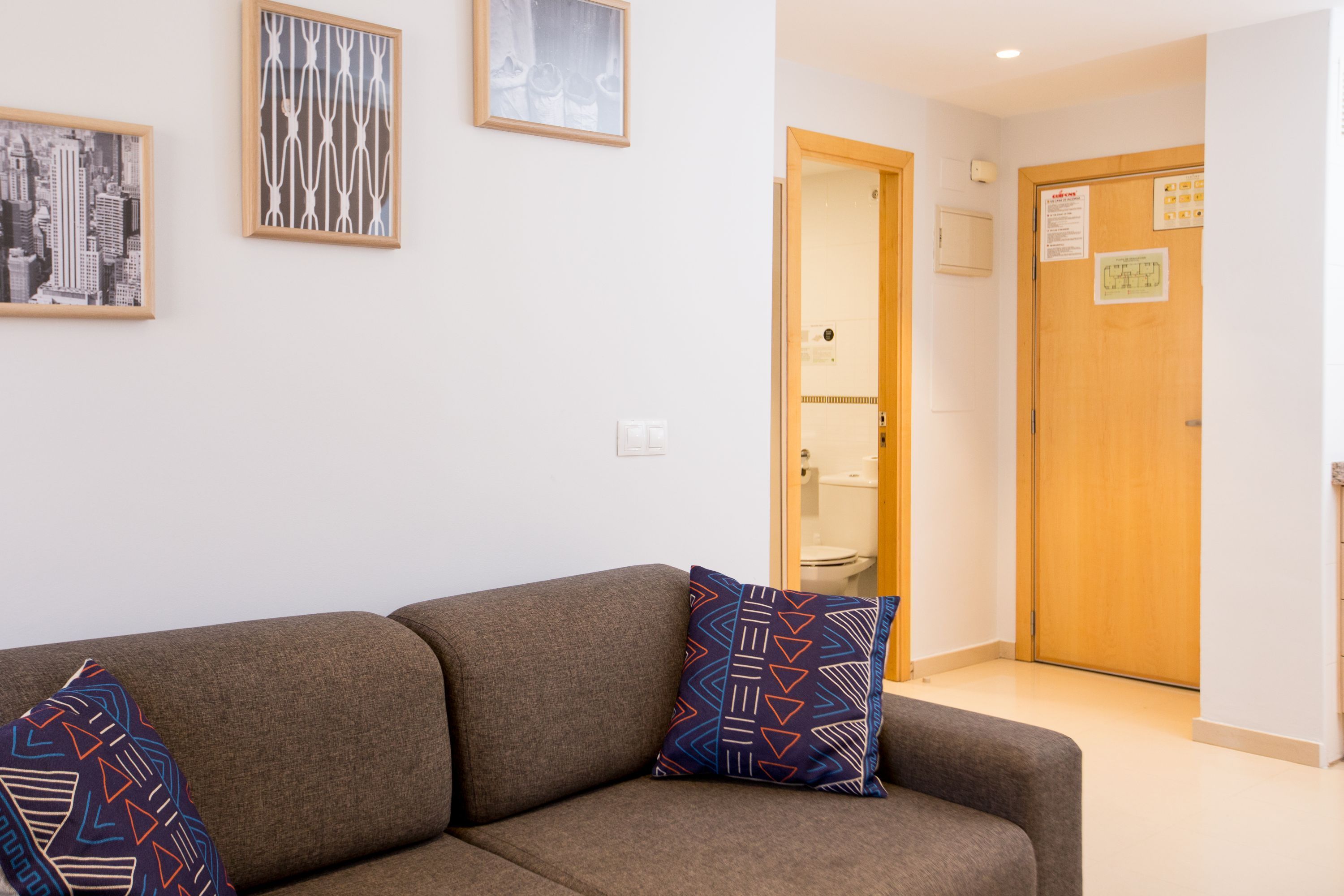 A modern hotel lobby with a sofa, framed artwork, and a wooden door.
