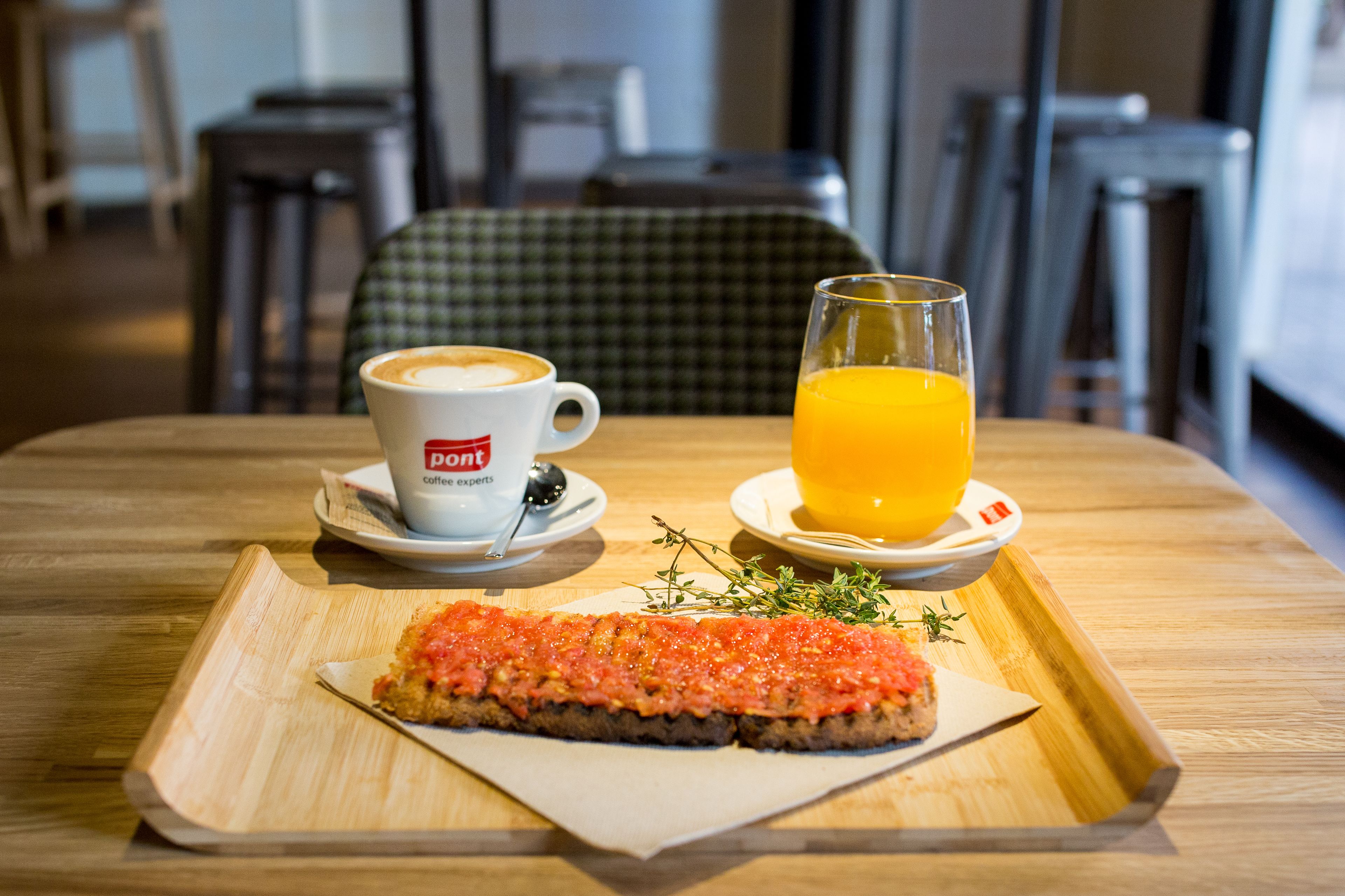 Une table en bois sur laquelle se trouve un plateau de petit-déjeuner avec un croissant, une tasse de café et un verre de jus d’orange.