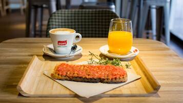 Une table en bois sur laquelle se trouve un plateau de petit-déjeuner avec un croissant, une tasse de café et un verre de jus d’orange.