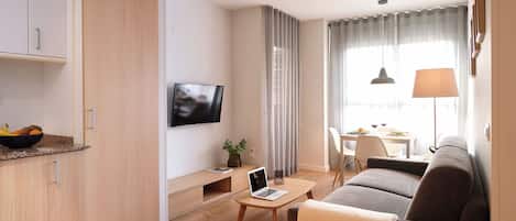 Una sala de estar moderna con un sofá, una mesa de centro, un televisor y una zona de comedor con una mesa y sillas.