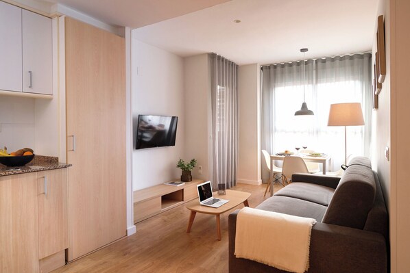 Una sala de estar moderna con un sofá, una mesa de centro, un televisor y una zona de comedor con una mesa y sillas.