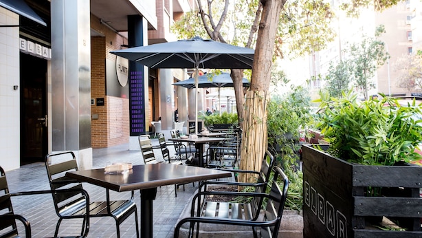 Een terras met tafels en stoelen, parasols en een houten plantenbak met groen.