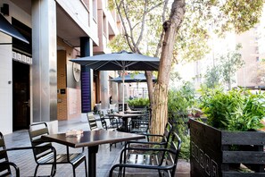 Un espace extérieur aménagé avec des tables et des chaises, des parasols et un bac à fleurs en bois agrémenté de plantes vertes.