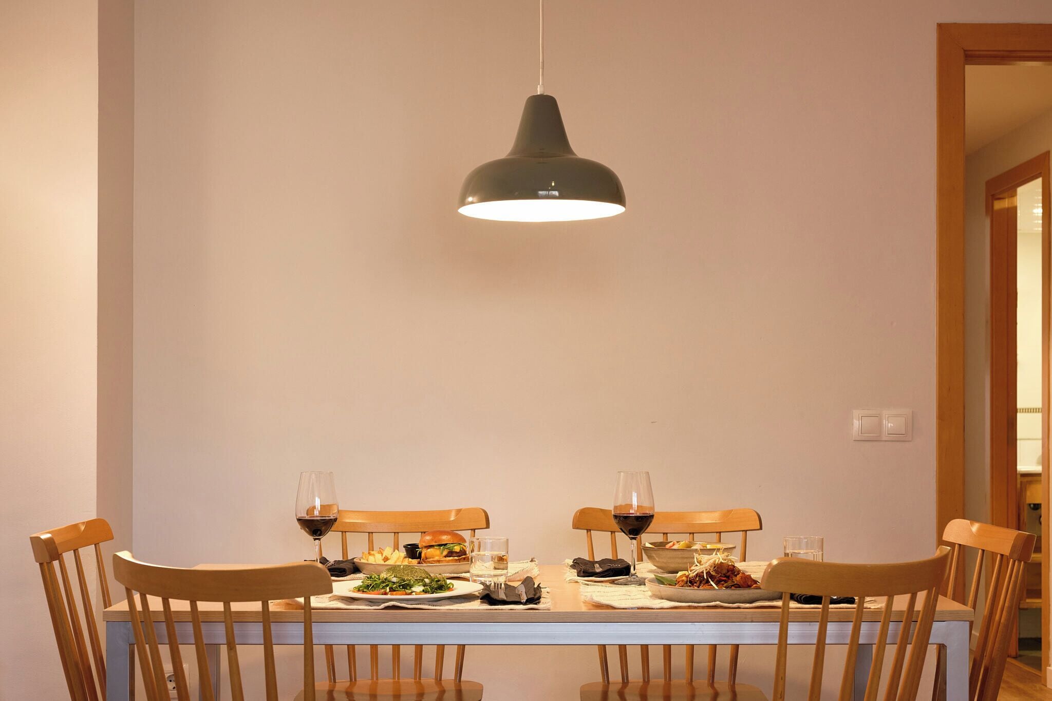 A dining table with chairs, a hanging light fixture, and a meal set.