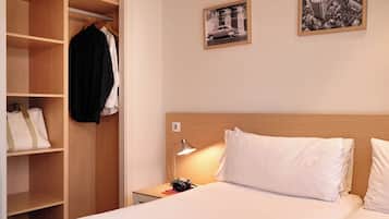 Une chambre d’hôtel bien rangée, avec un lit, une table de chevet, un bureau, une armoire et deux tableaux encadrés accrochés au mur.