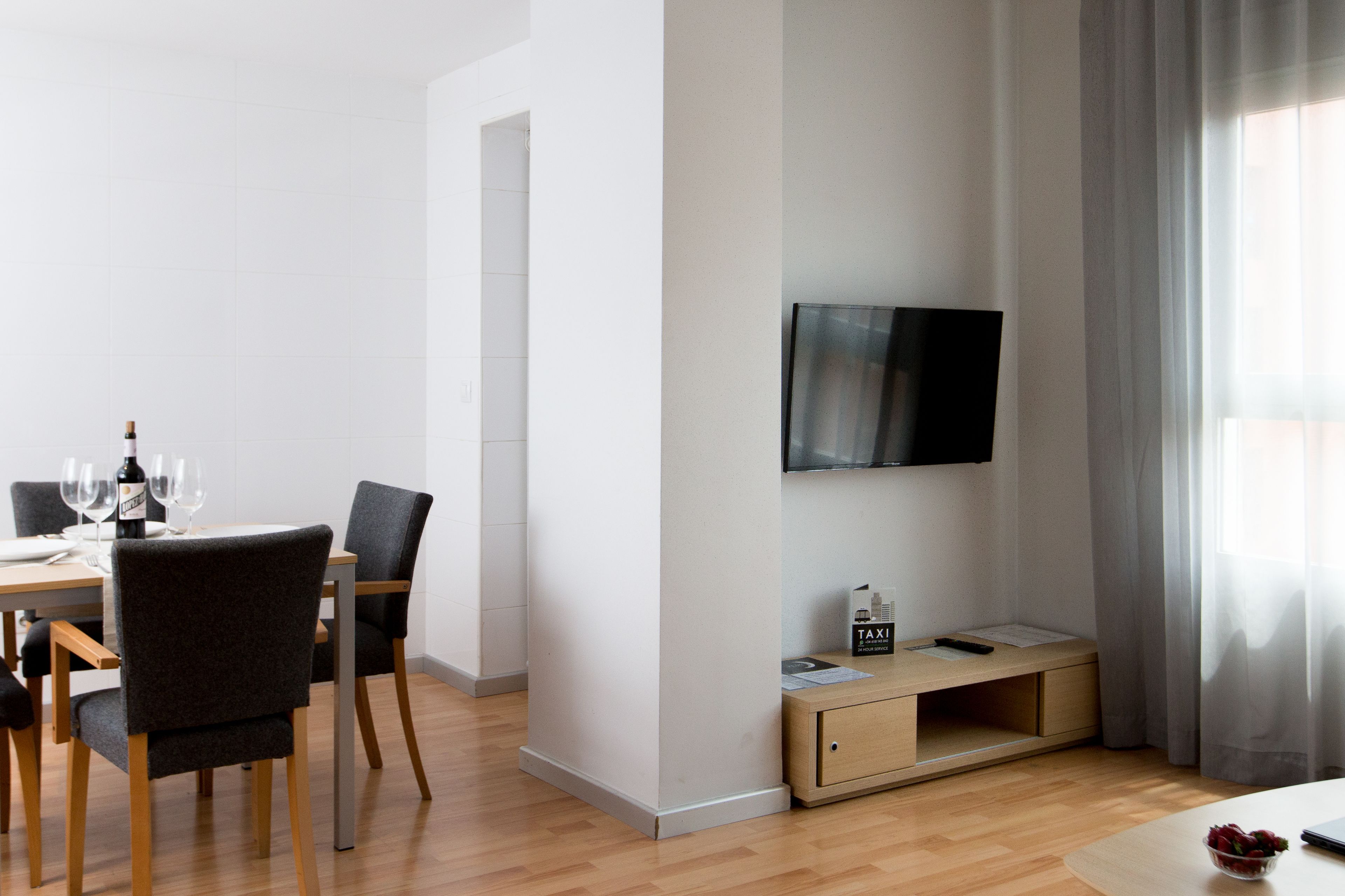 A modern living room with a dining area, a flat-screen TV mounted on the wall, and a wooden coffee table.