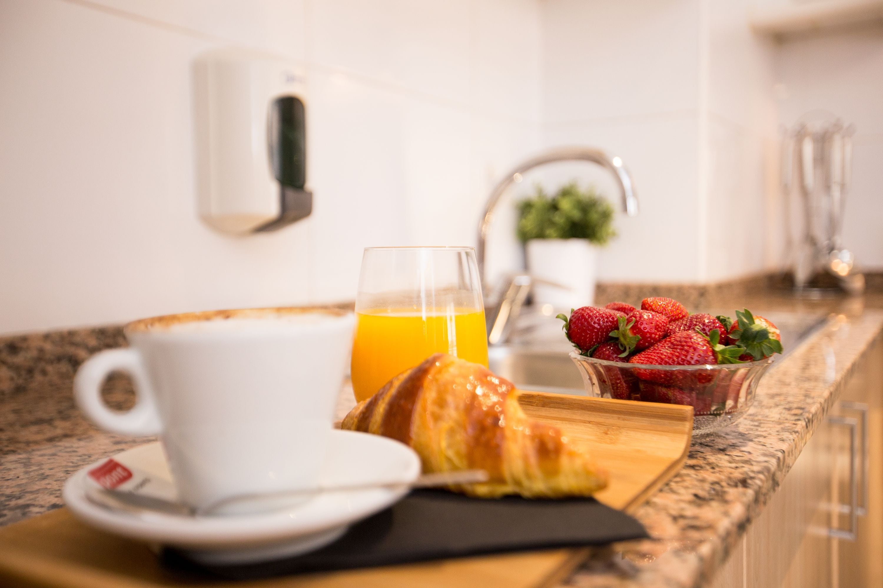 Ein Frühstückstisch mit Tasse, Orangensaftglas, einem Croissant und einer Schale Erdbeeren auf einer Küchenarbeitsfläche.