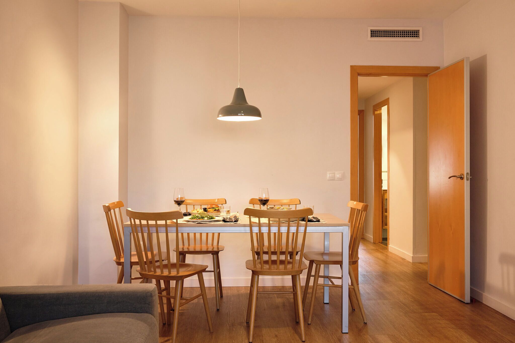 Un coin repas avec une table dressée pour quatre personnes, des chaises en bois et une suspension.