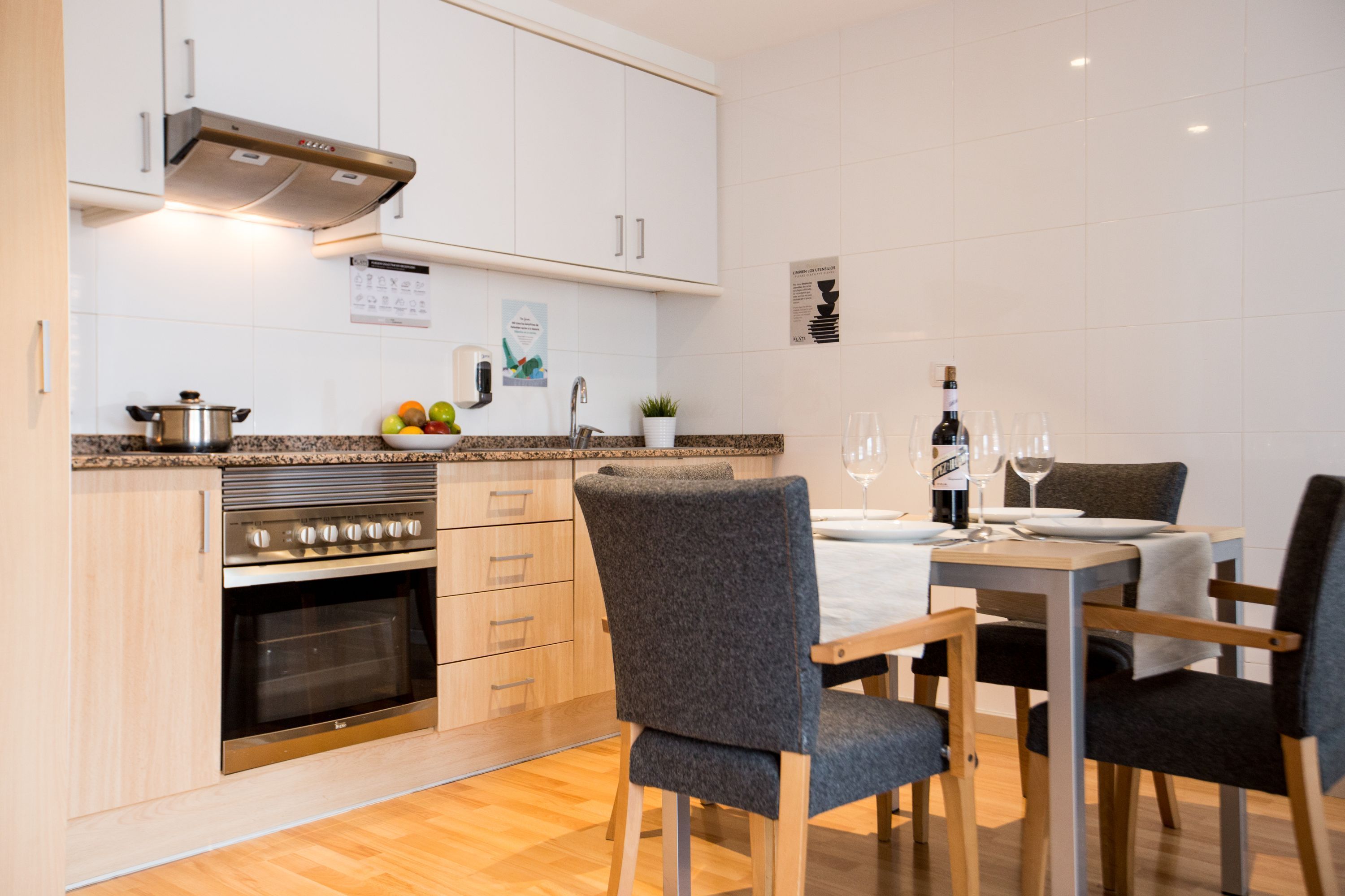 A modern kitchen with white cabinets, a built-in oven, granite countertop, and a dining area with a table and chairs.