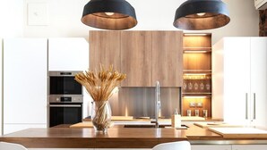 Una cocina moderna con una isla de madera, sillas blancas e iluminación colgante.