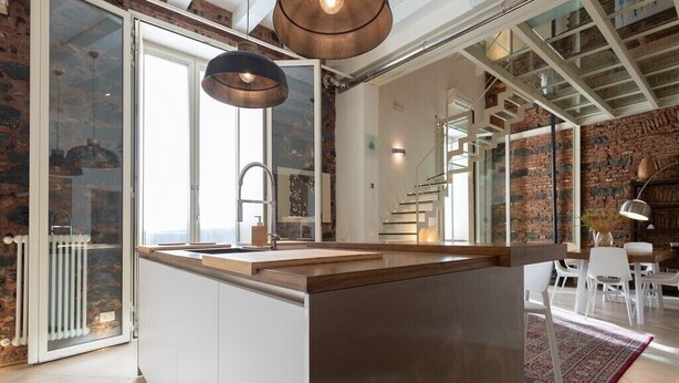 Una cocina moderna con una isla central, iluminación colgante y vistas al salón.
