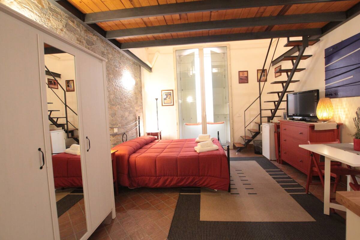 A compact hotel room with a bed, a desk, a chair, a TV, and a staircase.