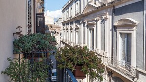 Una calle estrecha flanqueada por edificios, una planta en maceta en un balcón y un coche estacionado.