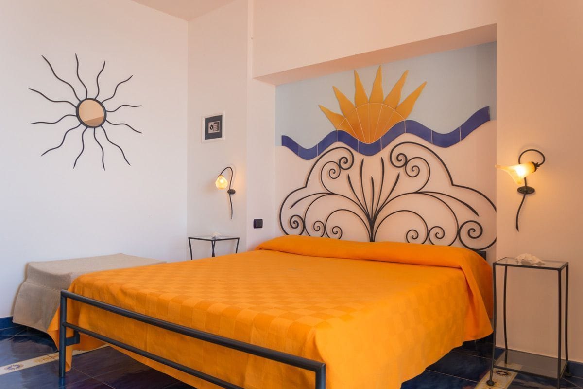 Une chambre à coucher comprenant un lit, un élément décoratif en forme de soleil fixé au mur, une tête de lit décorative et deux lampes de chevet.