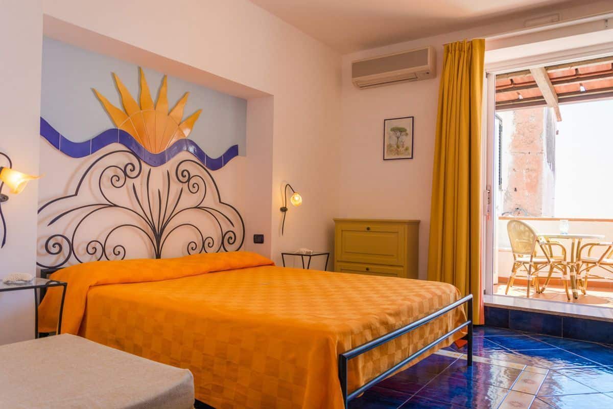 A room with a bed, a desk, a chair, a yellow cabinet, and a view of the outside.