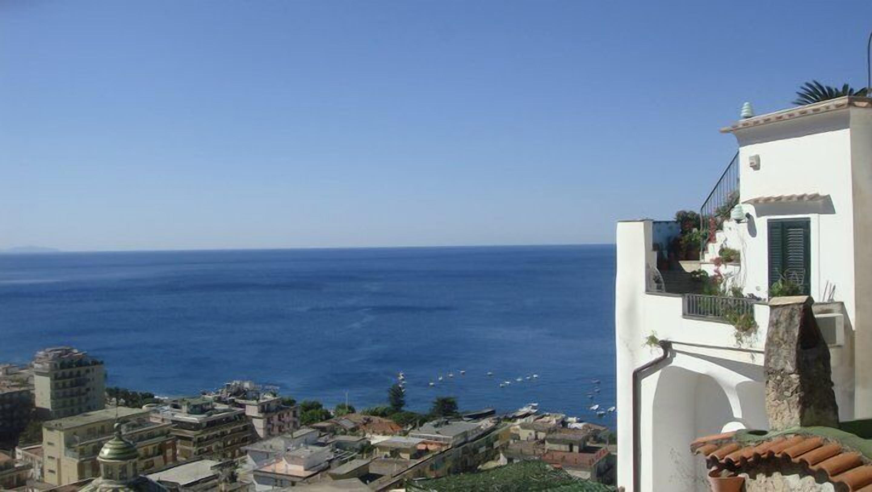 A coastal town with white buildings, a clear blue sea, and boats in the distance.