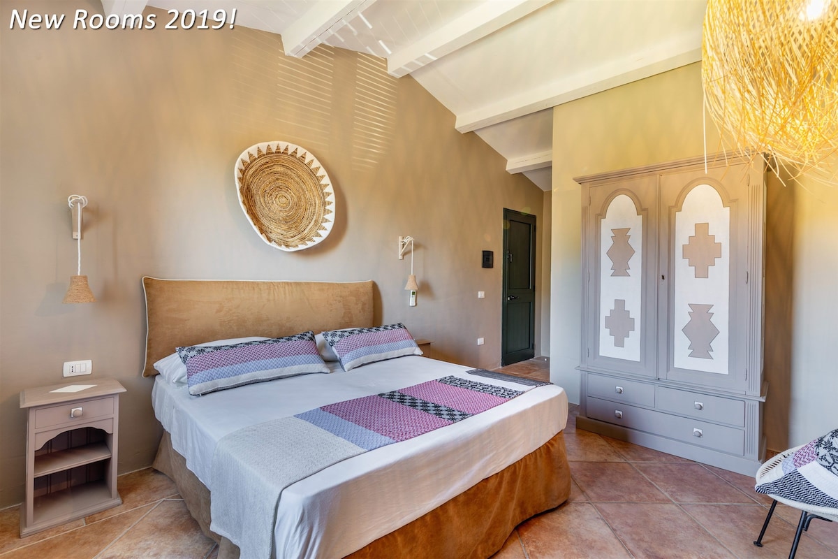 A bedroom with a bed, bedside table, lamp, wardrobe, and a decorative wall piece.
