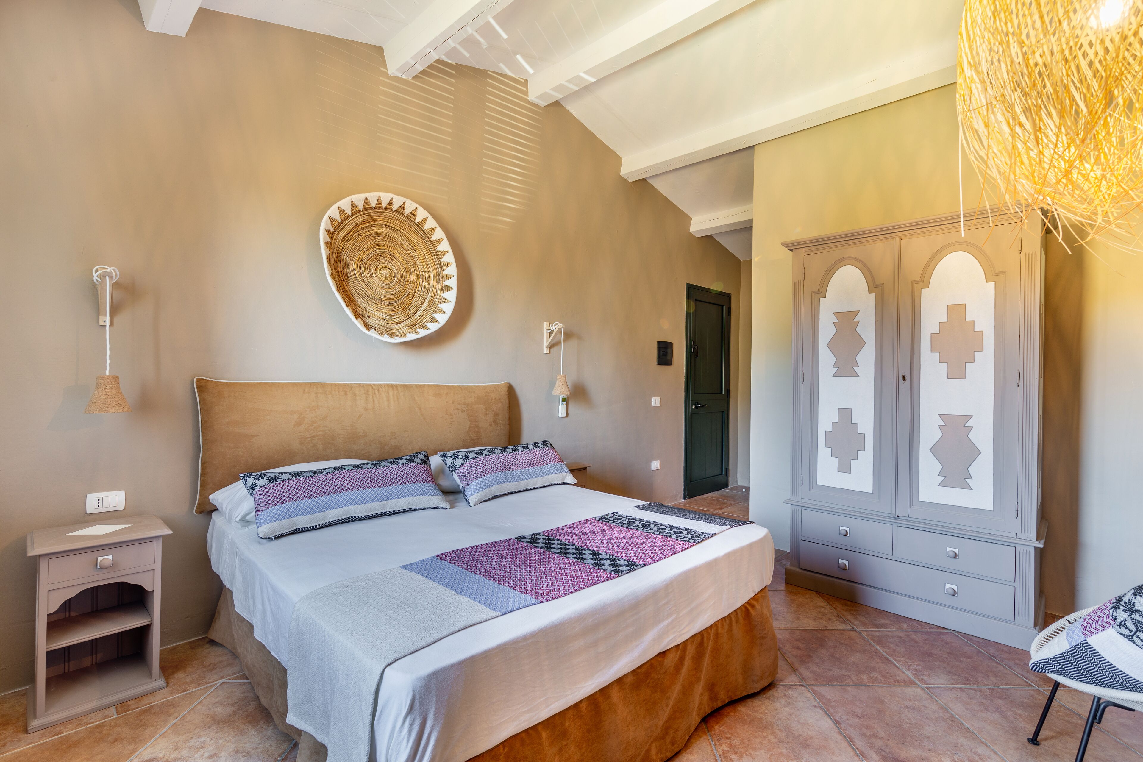A bedroom with a bed, nightstand, wall decor, wardrobe, and a hanging light fixture.