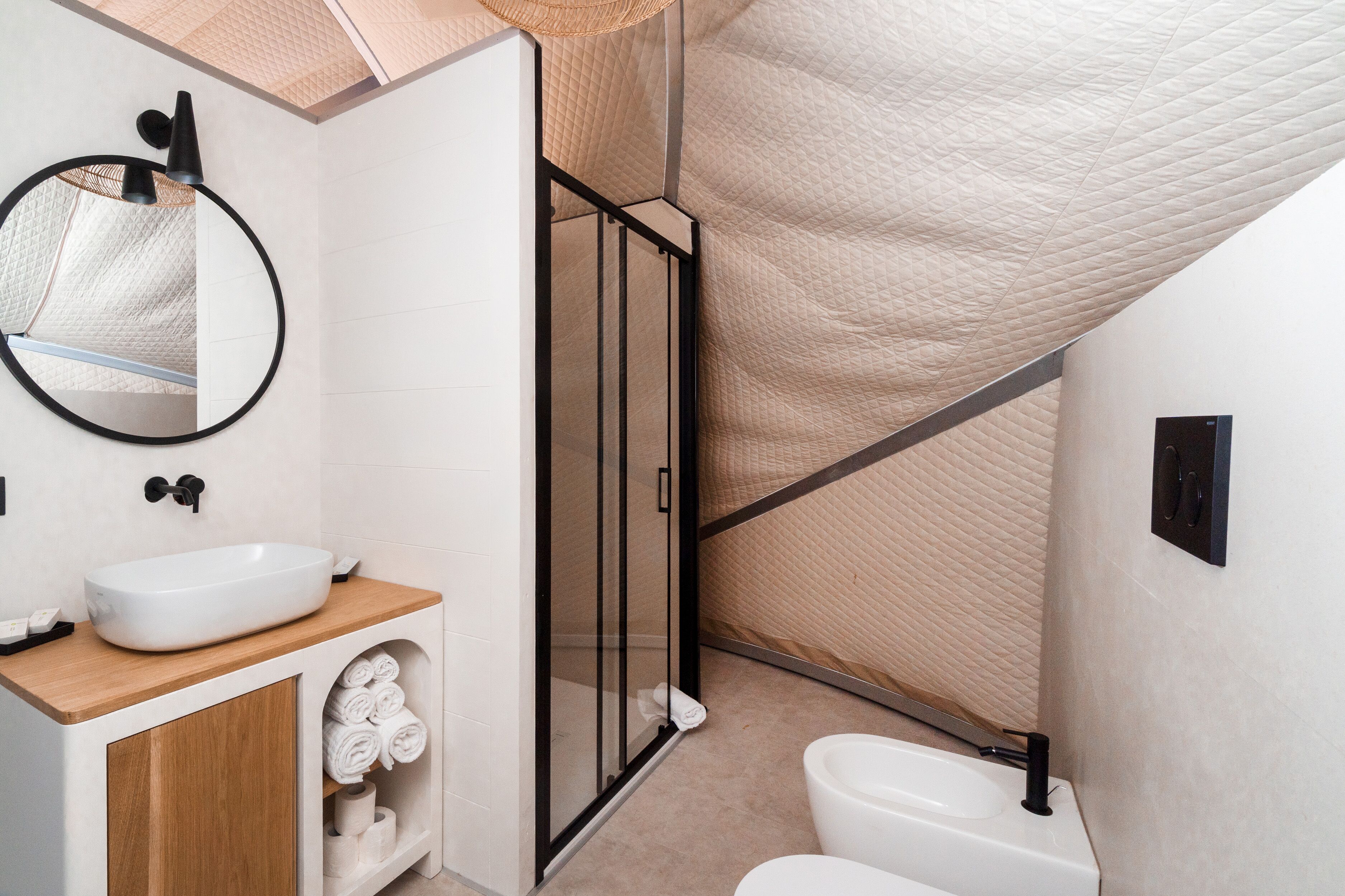 A modern bathroom with a white sink, wooden vanity, glass shower enclosure, and a toilet.