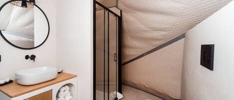 A modern bathroom with a white sink, wooden vanity, glass shower enclosure, and a toilet.