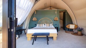 A tented room with a bed, bench, hanging lamps, and a wicker chair. - Hotel Glamping Borgo di Campagna (Loiri Porto San Paolo)