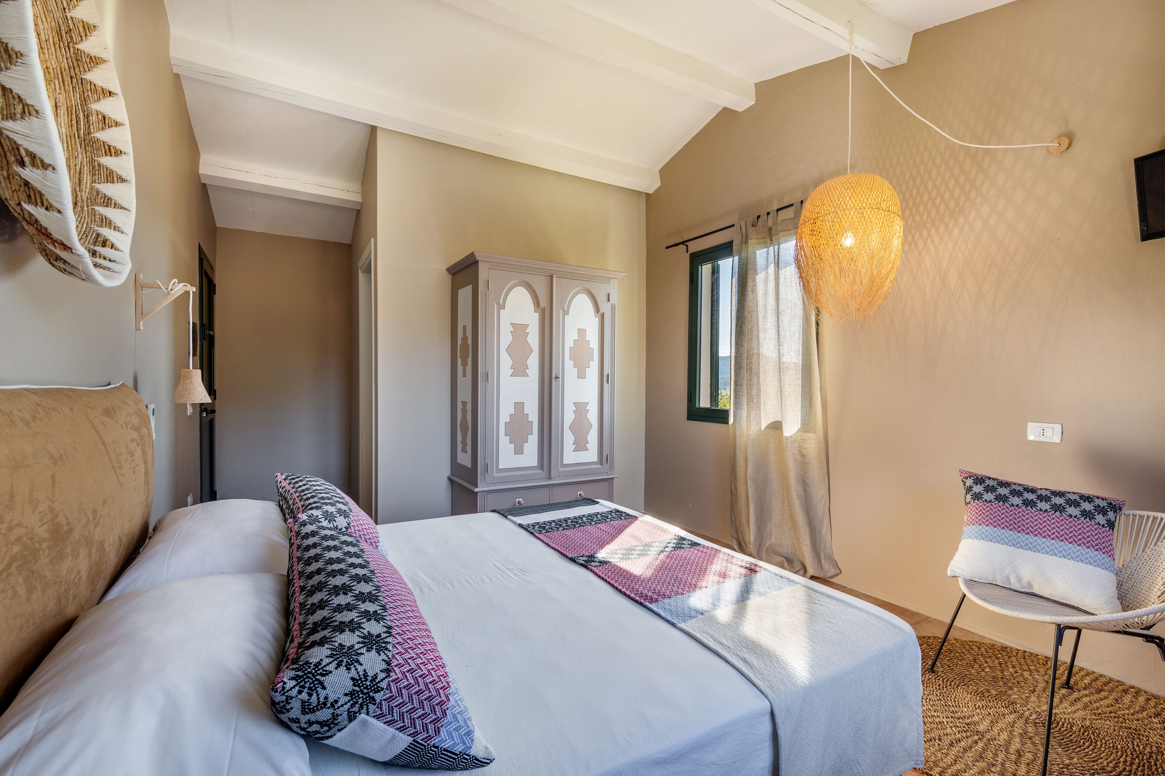 A bedroom with a bed, a wardrobe, a chair, and a hanging light fixture.