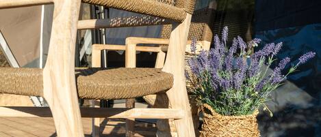 Wicker chairs and a woven basket with lavender plants on a wooden deck.