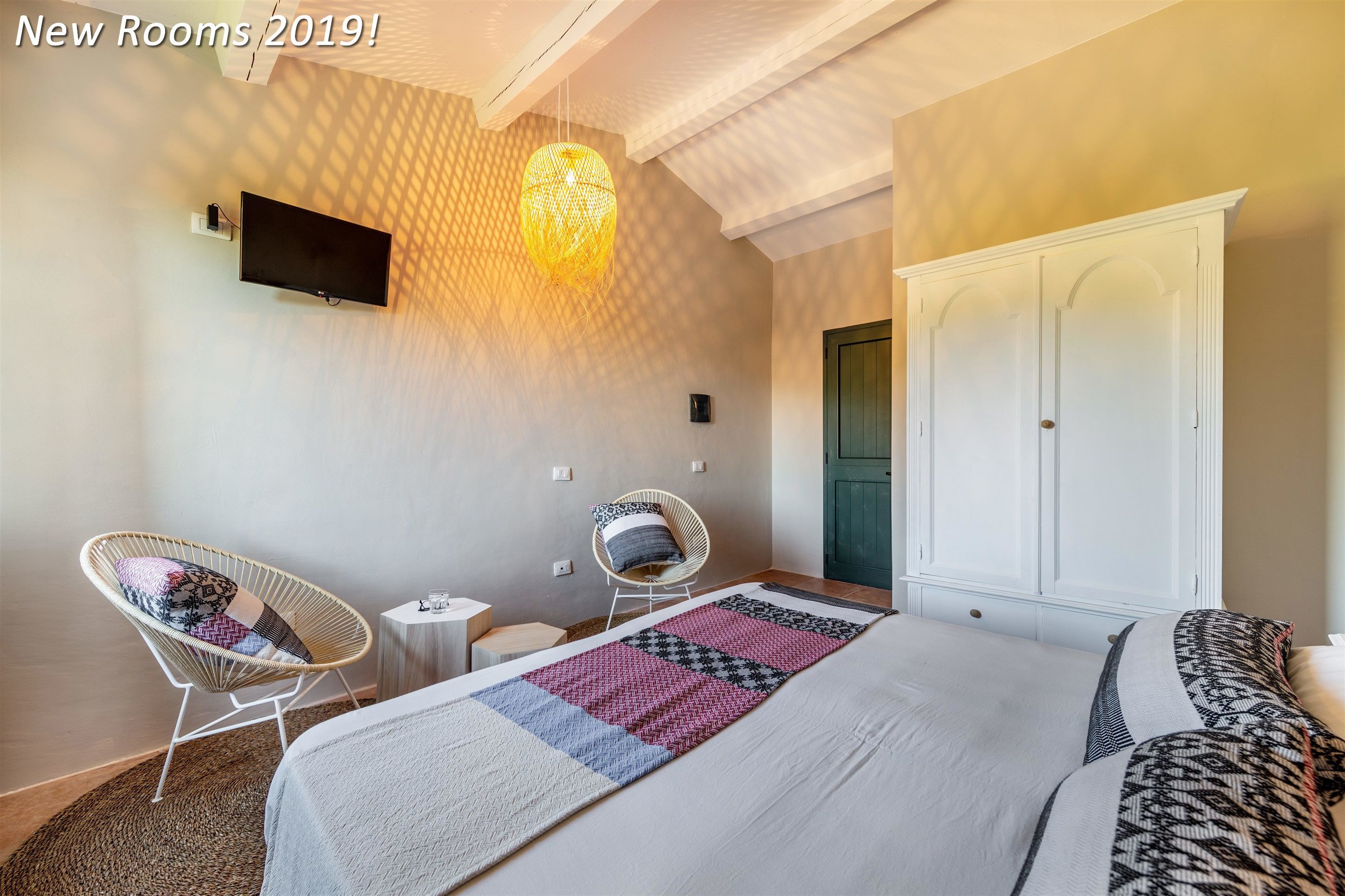 Ein modernes Hotelzimmer mit einem großen Bett, zwei Sesseln, einem Fernseher und einem Kleiderschrank.