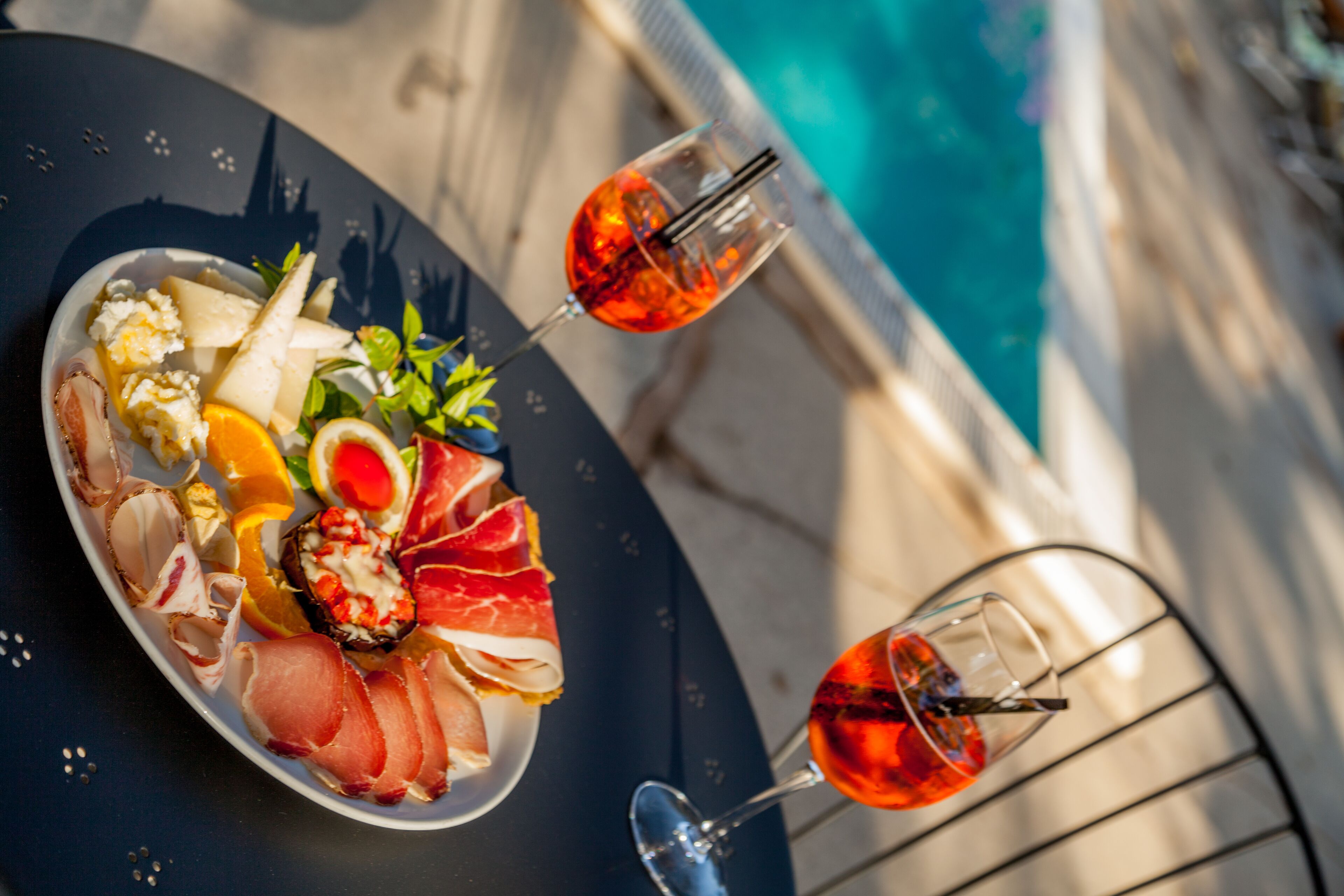 A seafood platter with various items and two glasses of red wine on a table by a pool.