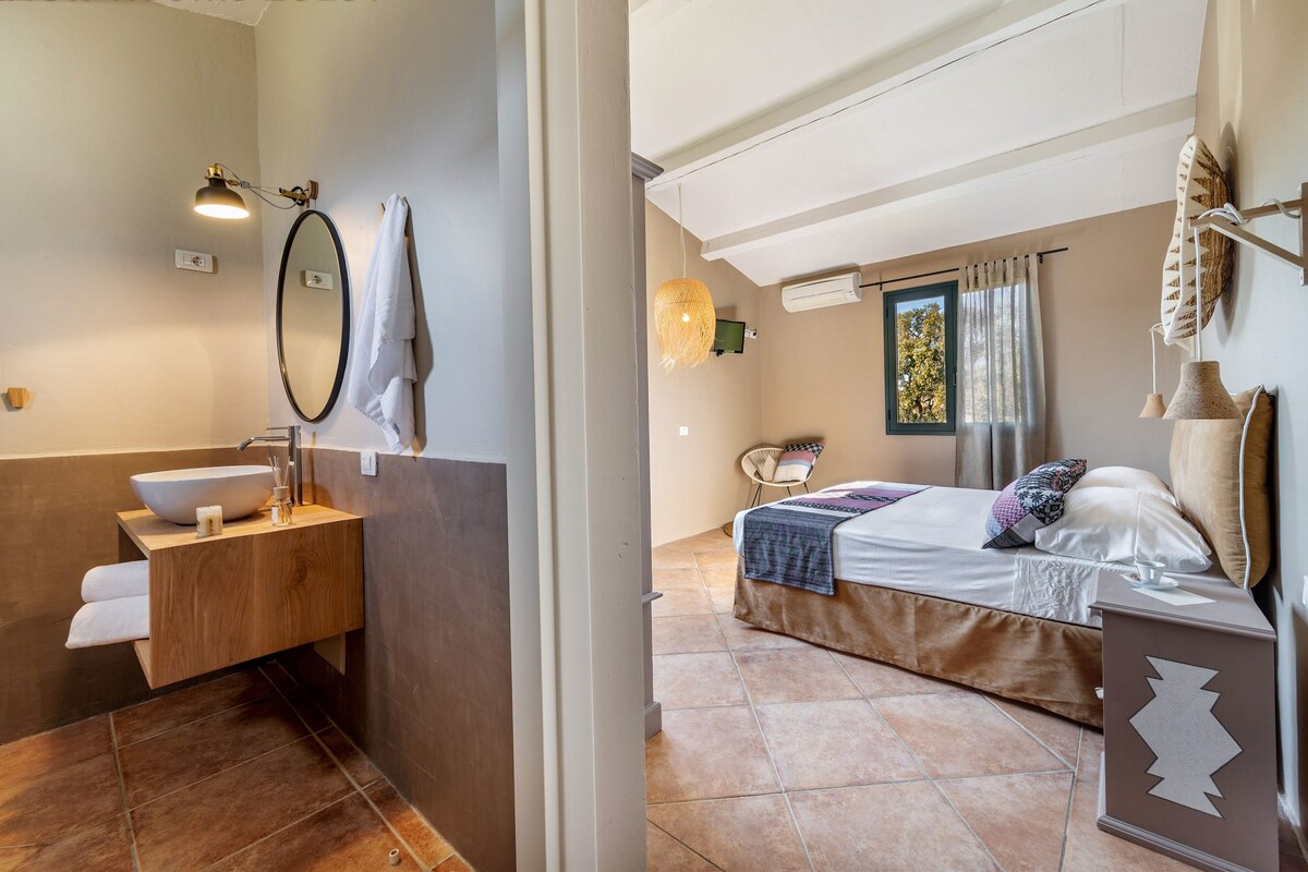 A modern bathroom with a freestanding sink, a large mirror, and a towel rack. The bedroom features a bed with a headboard, a bedside table, and a window with curtains.