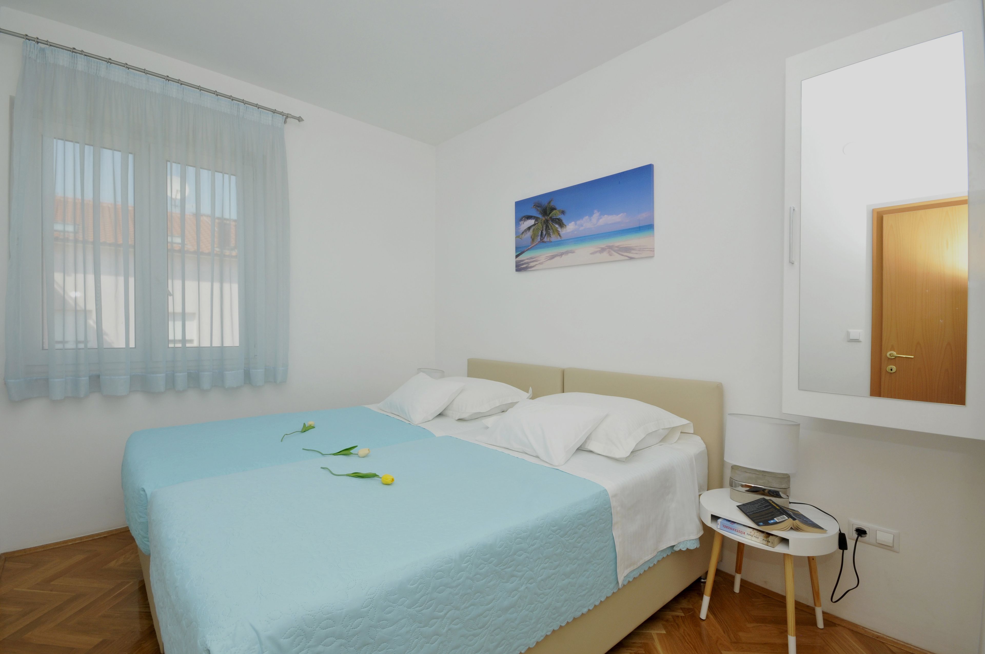 Et soveværelse med en seng, et lille natbord, et billede på væggen og et vindue med let gardin.