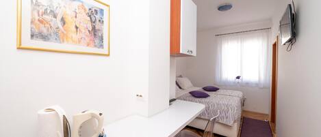 A hotel room with a bed, a desk with a chair, a painting on the wall, and a bathroom visible through an open door.