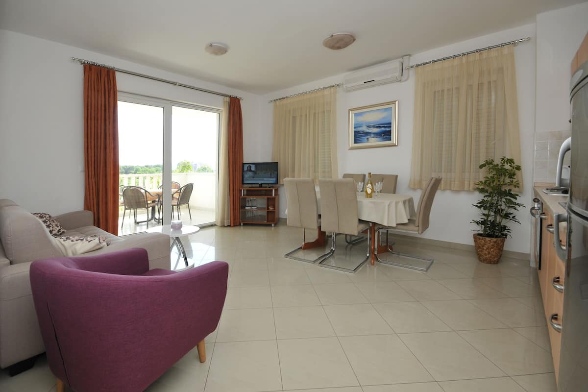 Una sala de estar moderna con un sofá, un sillón morado, una mesa de comedor con sillas, un televisor y una planta en maceta.