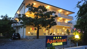 A multi-story building with balconies, a sign reading "Apartmani Trogir," and a car parked in front. - Apartmani Trogir (Trogir)