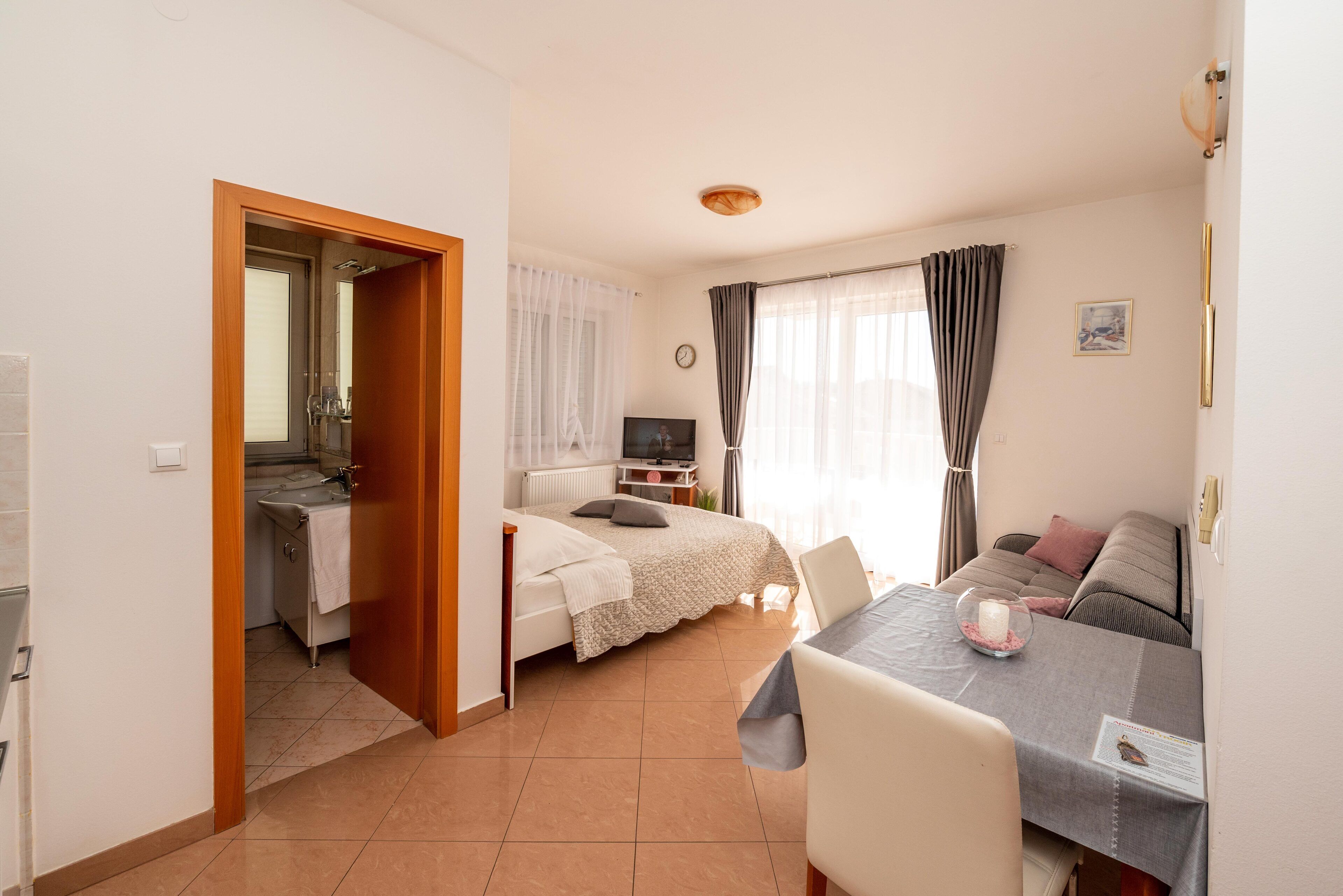 Ein Hotelzimmer mit Bett, Fernseher, Esstisch mit Stühlen, einer kleinen Küchenzeile und einem Badezimmer.