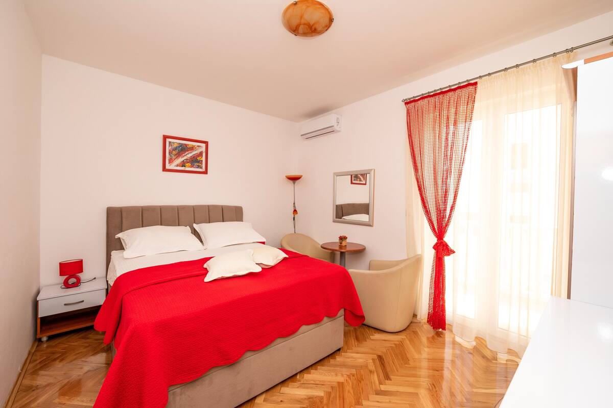 Un dormitorio con cama, mesita de noche, silla y ventana con cortinas.