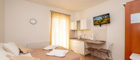 A bedroom with a bed, a desk, and a chair. There is a window with curtains, a clock, and a picture on the wall.