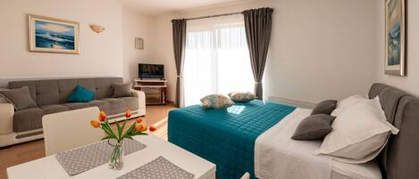Una habitación luminosa con cama, sofá, televisor y comedor con mesa y sillas.